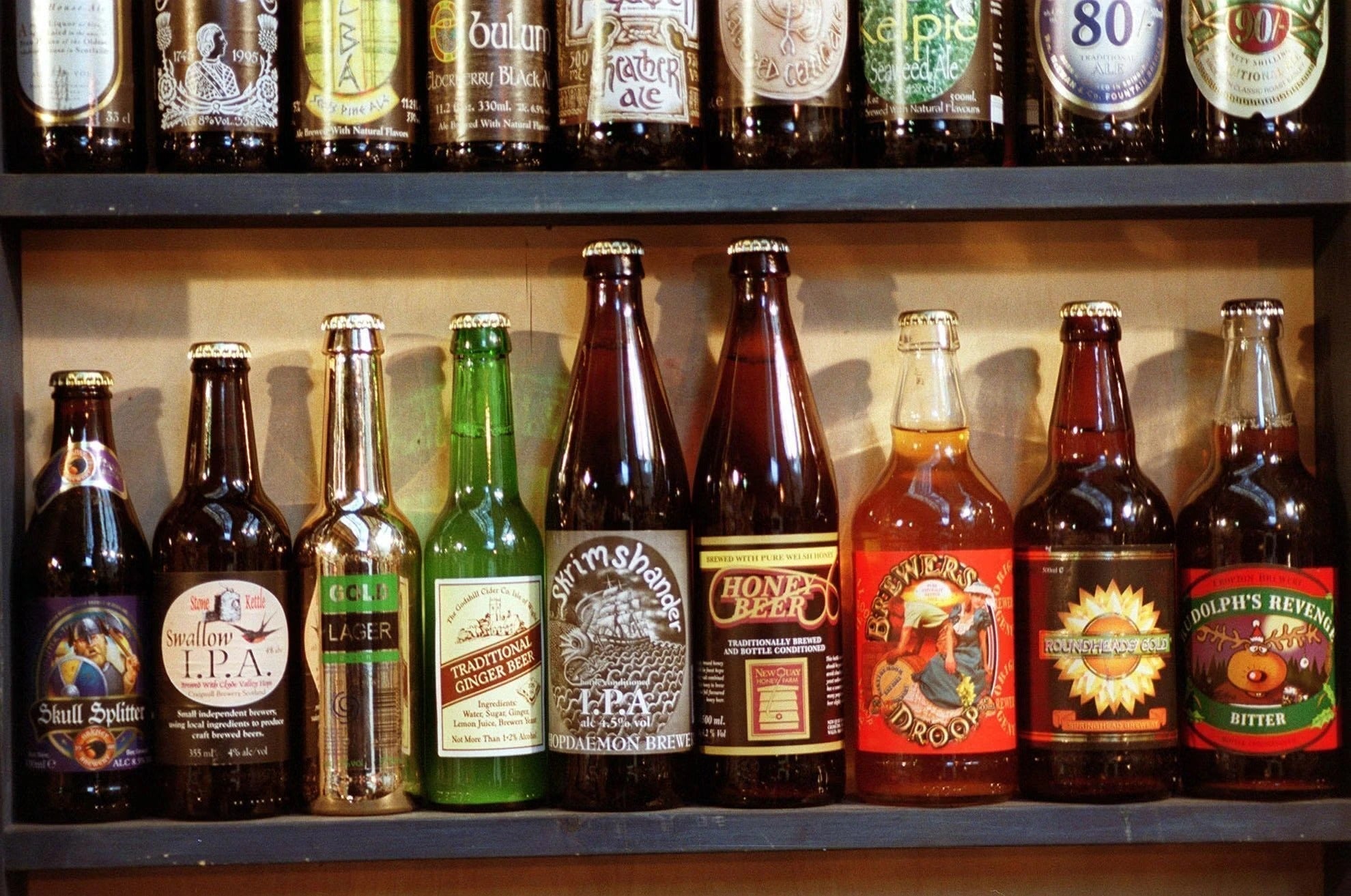 A wooden shelf lined with various craft beer bottles, representing a typical birthday present. The article suggests swapping this standard choice for a unique custom video game gift for friends.